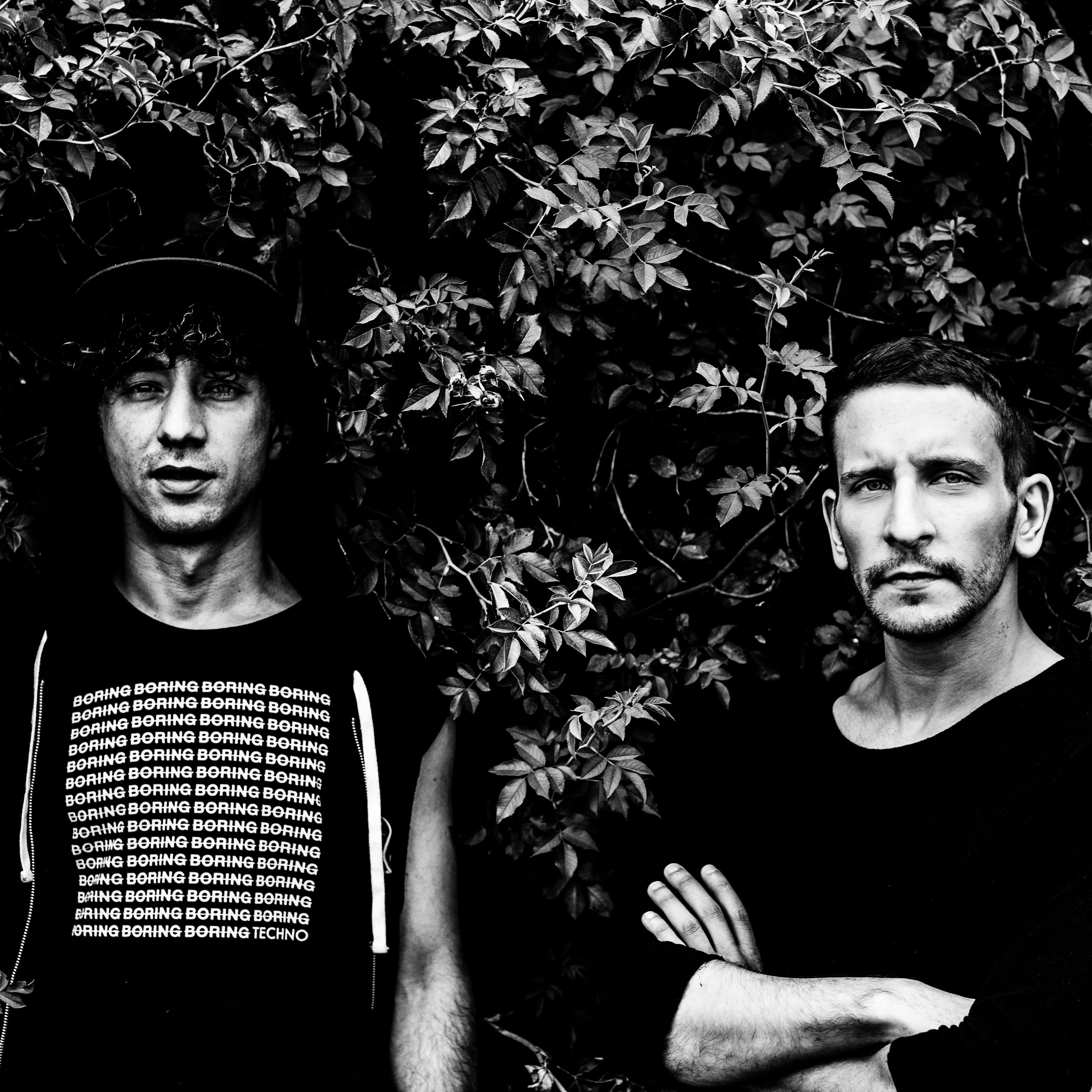 Two men standing against a leafy background